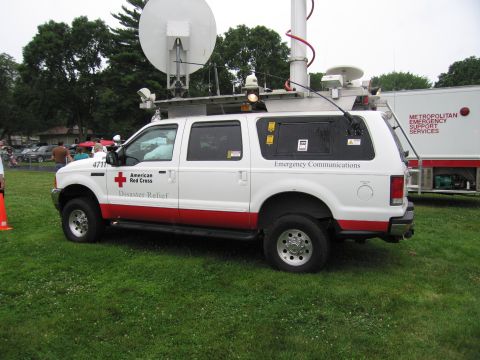 1991 Ford Crown Victoria - A white and red truck with American Red Cross markings and emergency communications equipment is parked on grass next to a trailer.