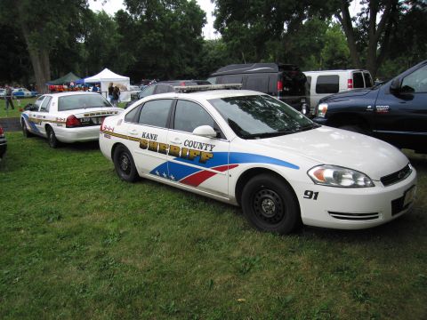 1991 Ford Crown Victoria - A white police car with 'KANE COUNTY SHERIFF' text and graphics is parked on grass, with another police car visible in the background.