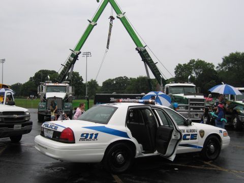 1991 Ford Crown Victoria - A police car is parked with its doors open, alongside other vehicles and a large crane.