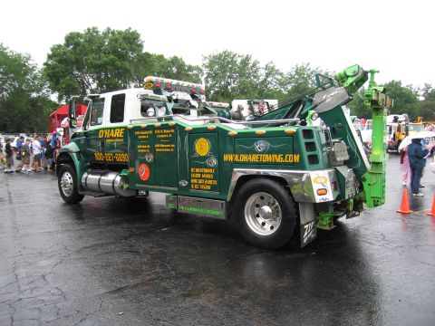 1991 Ford Crown Victoria - A green and white tow truck is parked on a wet surface, with people and other vehicles in the background.