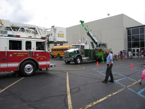 1991 Ford Crown Victoria - A fire truck, tow truck, and school bus are visible in a parking lot with a crowd of people in the background.