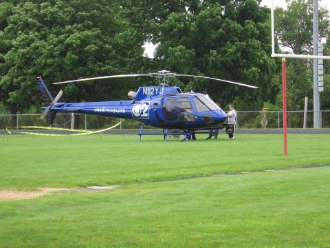 1991 Ford Crown Victoria - A blue helicopter with registration N12YJ and CBS Chicago logo is parked on a grass field.