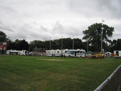 1991 Ford Crown Victoria - Multiple white mobile command center vehicles are parked on a grassy field under a cloudy sky.