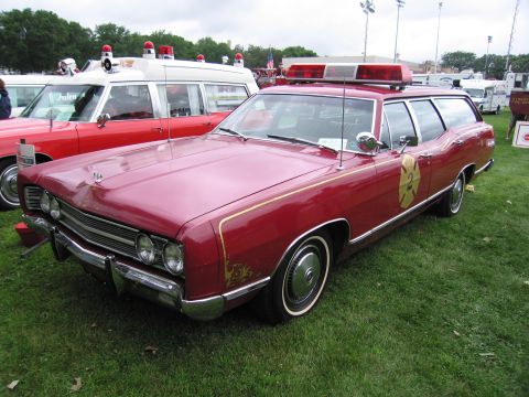 1991 Ford Crown Victoria - A red 1969 Ford Country Sedan station wagon is parked on grass next to an ambulance.