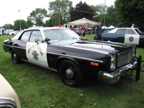 1991 Ford Crown Victoria - A 1977 police car is shown parked on a grassy field with other vehicles and tents in the background.