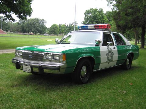 1991 Ford Crown Victoria - This 1991 Ford Crown Victoria police car is parked on a grassy field with trees in the background.