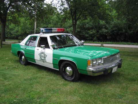 1991 Ford Crown Victoria - This green and white sheriff's car features a light bar and a distinctive 1980s body style, not matching the 1991 Ford Crown Victoria claim.