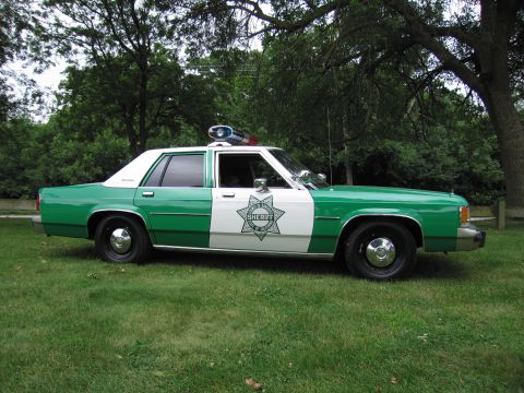 1991 Ford Crown Victoria - This sheriff car, likely from the 1980s, is parked on a grassy area with trees providing shade.