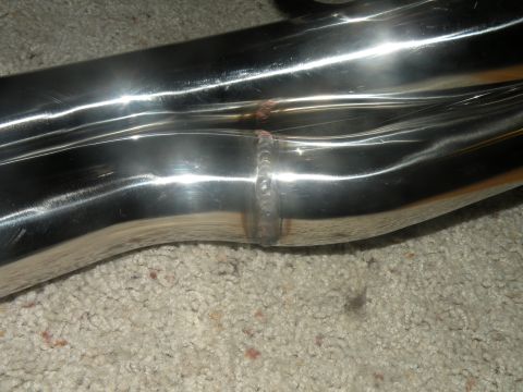 1998 Subaru Legacy - Shiny metal exhaust manifold pipe with visible welds, resting on a carpeted surface.
