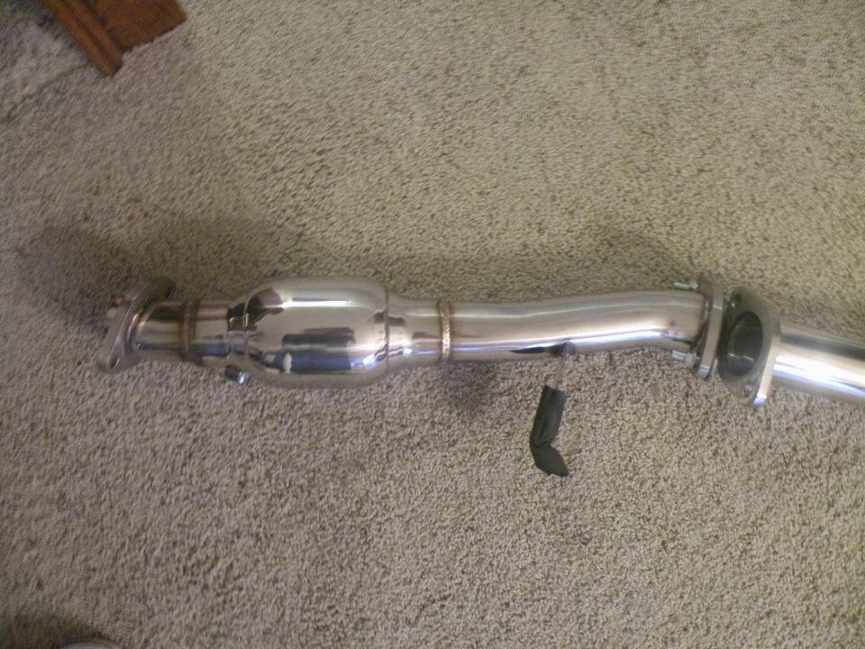 Chrome exhaust pipe with a catalytic converter section, lying on a carpeted surface