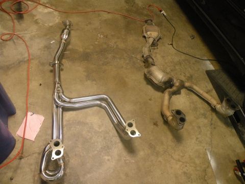 1998 Subaru Legacy - Two exhaust systems, one new and one used, are laid out on a concrete floor, possibly for comparison or installation.