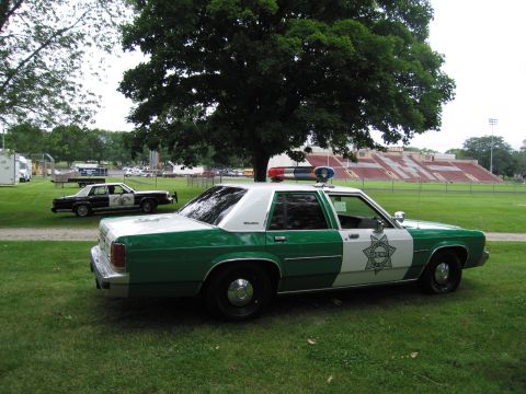 1991 Ford Crown Victoria - A green and white 1991 Ford Crown Victoria police car is parked on a grassy field with another police car in the background.