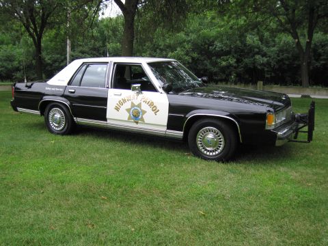 1991 Ford Crown Victoria - This 1991 Ford Crown Victoria police car is parked on a grassy area with trees in the background.