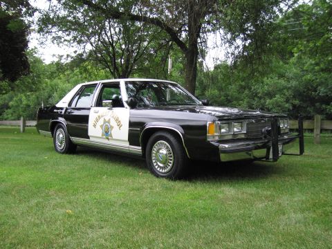 1991 Ford Crown Victoria - A black and white police car is parked on a grassy lawn with trees in the background.