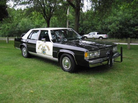 1991 Ford Crown Victoria - This 1991 Ford Crown Victoria, marked as a highway patrol vehicle, is parked on a grassy area with trees in the background.
