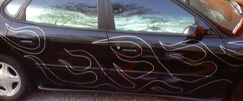 1999 Ford Taurus - A black sedan with silver flame decals is shown from the side. The vehicle's year is not discernible from the image.