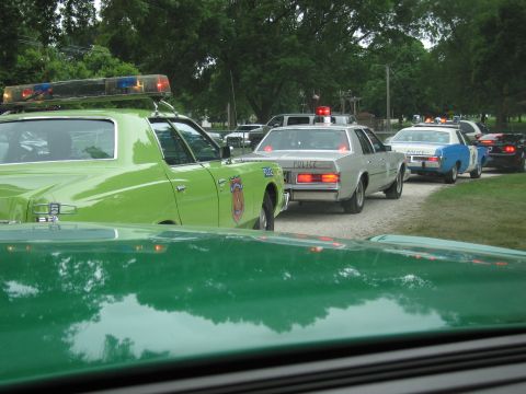 1991 Ford Crown Victoria - A procession of police vehicles, a distinctive green car with emergency lights, followed by several others.