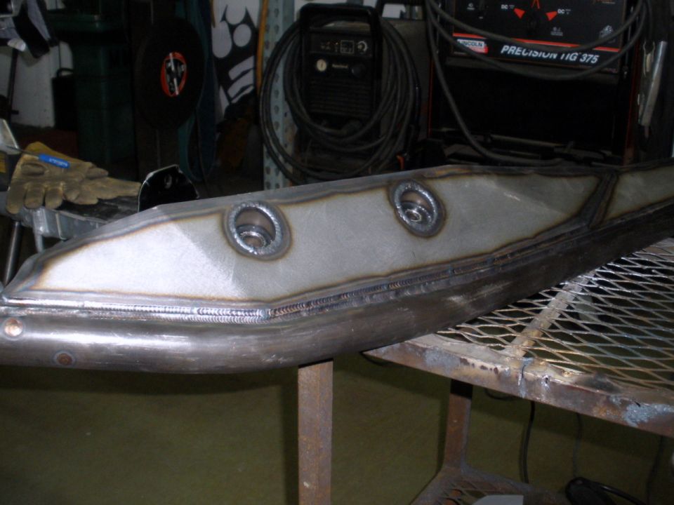 welded metal component with two circular openings, resting on a metal grate