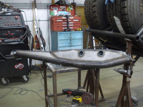 1995 Ford Bronco - Custom suspension part in a workshop, with welding equipment and tires in the background.