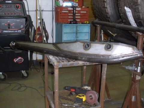 1995 Ford Bronco - A custom-fabricated suspension component rests on a metal table in a workshop, with welding and grinding equipment visible.