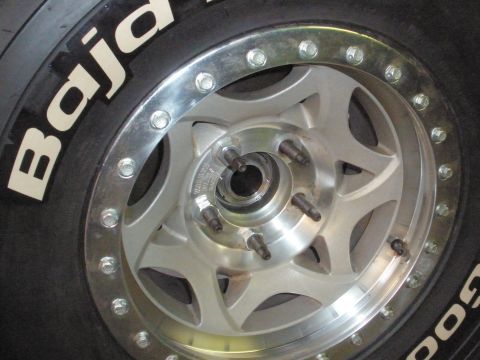 1995 Ford Bronco - A close-up view of a BFGoodrich Baja tire mounted on a silver aftermarket wheel, showing the lug nuts and wheel studs.