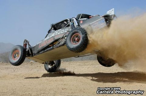 1989 Ford Bronco - Off-road buggy airborne, kicking up a cloud of dust during a race.