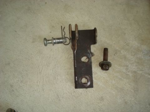 1990 Ford Bronco - A disassembled metal bracket assembly with a pin and bolt is shown on a textured surface.