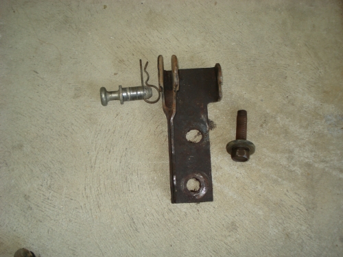 metal bracket with a pin and spring, plus a separate bolt, lying on a concrete surface