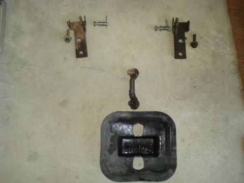 1990 Ford Bronco - Various vehicle parts are displayed on a concrete floor, including brackets and a metal plate.