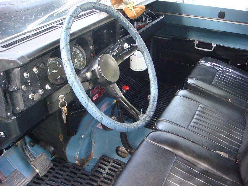 Land Rover interior with blue-wrapped steering wheel, black dash gauges, and black vinyl bench seat