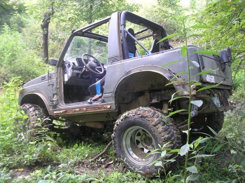 1987 Suzuki Samurai - This vehicle is parked on a muddy trail surrounded by trees, with its doors removed.
