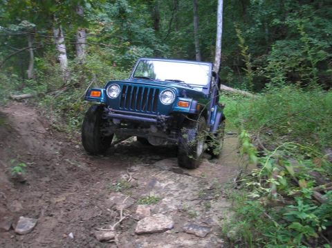 1987 Suzuki Samurai - This teal Jeep Wrangler tackles a challenging off-road course with mud and rocks.