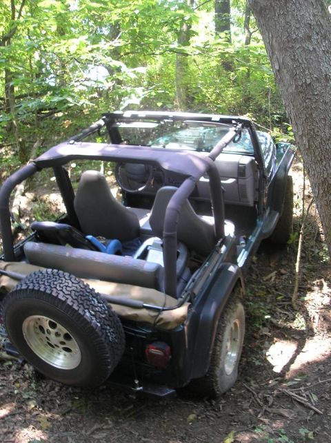 1987 Suzuki Samurai - A dark green Jeep Wrangler is parked off-road, partially obscured by trees and foliage.