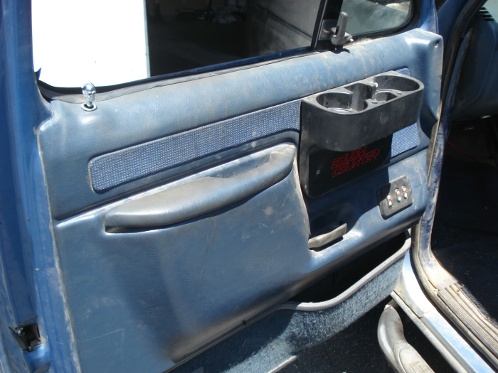 Blue Ford door panel with black aftermarket cup holder insert, armrest, and power window switches