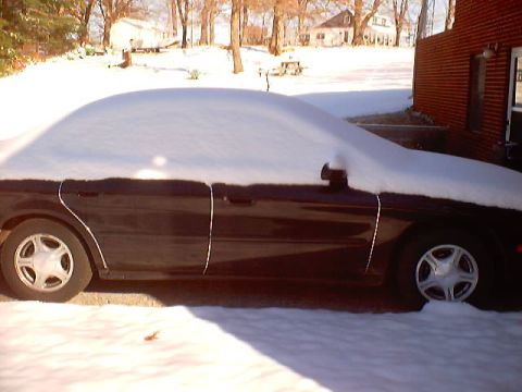 1999 Ford Taurus - A dark sedan sits covered in snow, partially obscuring its side profile and wheels.