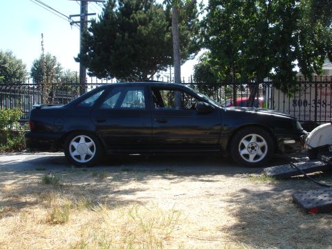 1991 Ford Taurus - Side view of a black sedan with a spoiler and alloy wheels parked outdoors.