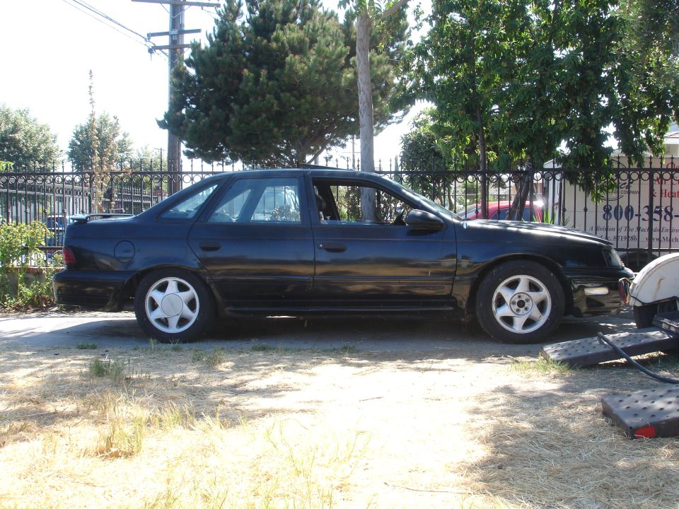 Black Ford Taurus SHO sedan parked on dirt by a fence with flat tire