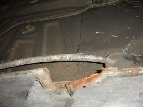 1991 Ford Taurus - The underbody of a vehicle displays significant rust and a cracked support structure, with a ribbed hose visible.