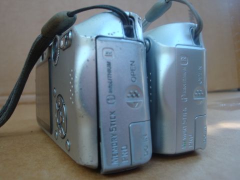 1993 Ford Taurus - Two silver digital cameras are shown from the side, with one slightly behind the other, revealing details like the memory stick slot and op…