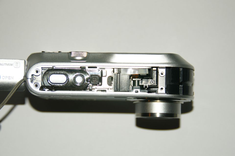 Silver digital camera with side panel removed, showing internal components and lens mount