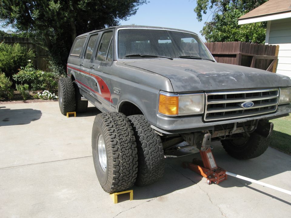 Gray Ford truck with dual rear wheels and large off-road tires, jacked up in a driveway