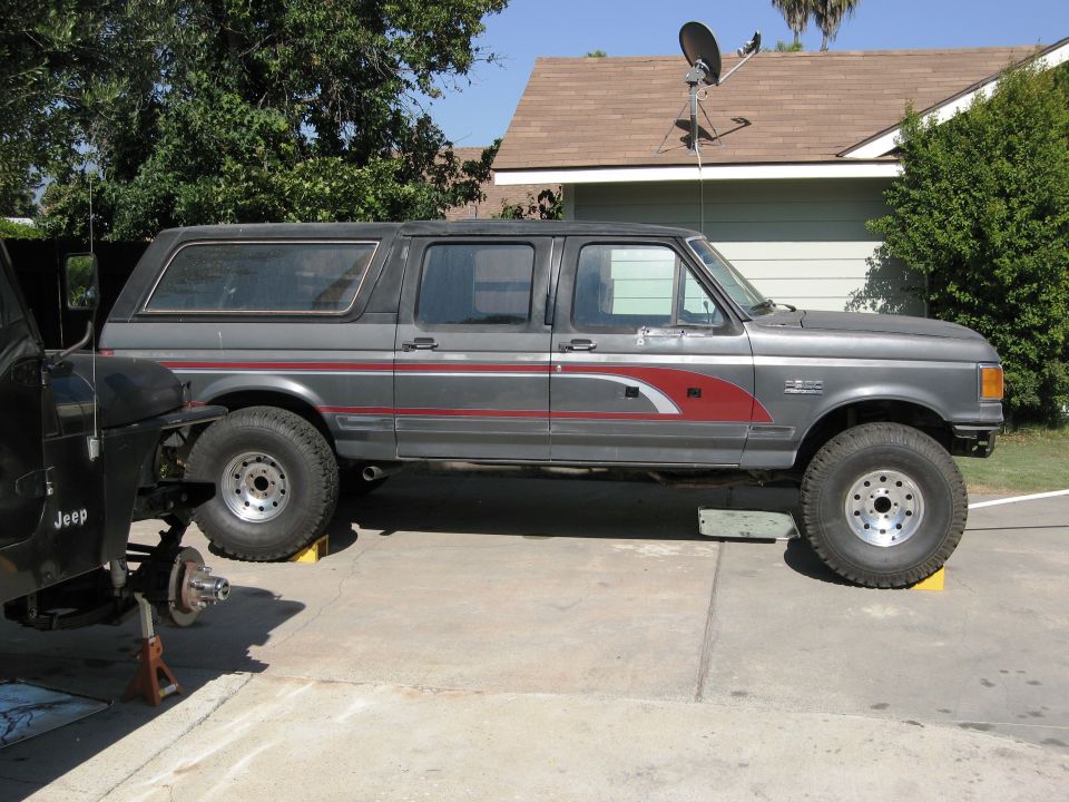 Gray Ford Bronco SUV with red stripe, lifted on yellow blocks, side view