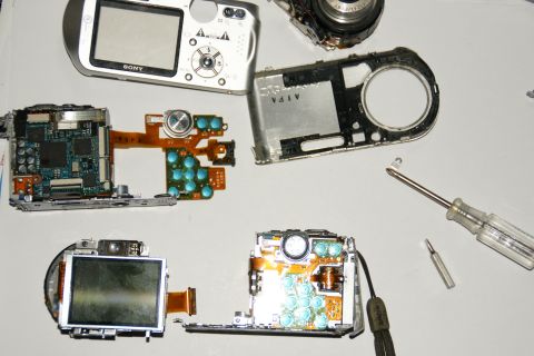 1993 Ford Taurus - Various parts of disassembled digital cameras are laid out on a white surface next to a screwdriver.