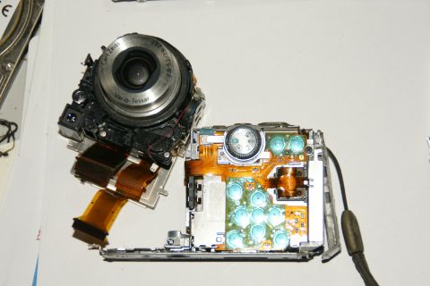 1993 Ford Taurus - A digital camera is shown disassembled, revealing its internal components including the lens assembly and circuit board with buttons.