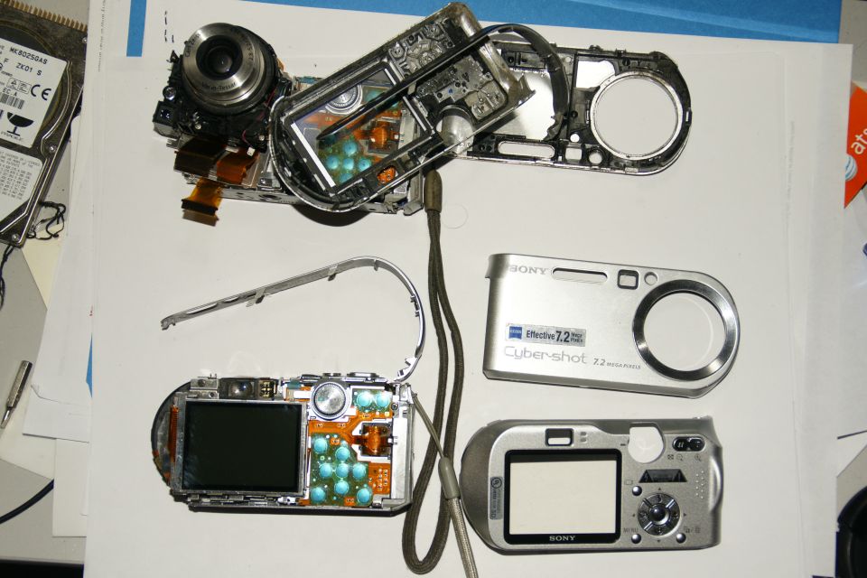 Disassembled Sony Cyber-shot digital cameras and a hard drive on a white surface