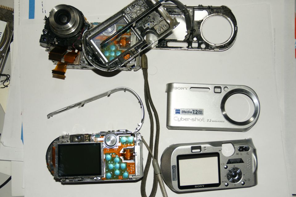 Disassembled Sony Cyber-shot digital cameras laid out, showing internal components and exterior parts
