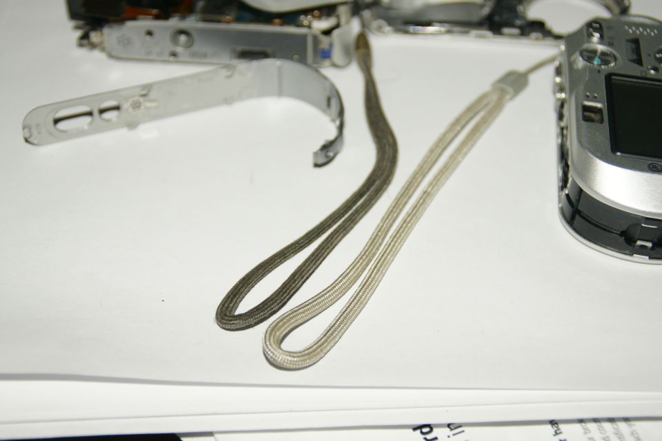 Disassembled silver digital camera with two wrist straps on white paper