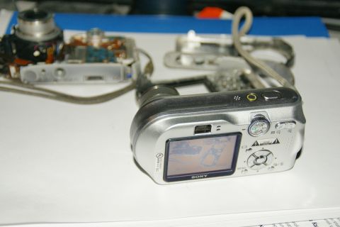 1993 Ford Taurus - A silver Sony digital camera is shown disassembled, with its internal components exposed on a white surface.