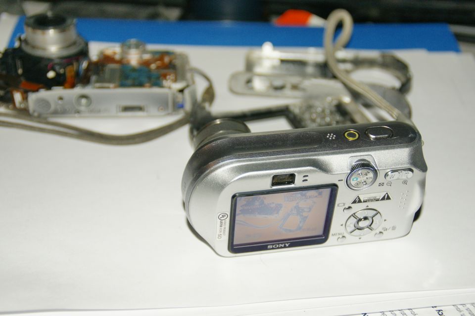 Disassembled silver Sony digital camera on a white surface