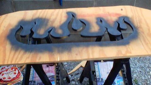 1999 Ford Taurus - A wooden board with a flame-shaped stencil is being spray-painted, with some overspray visible.